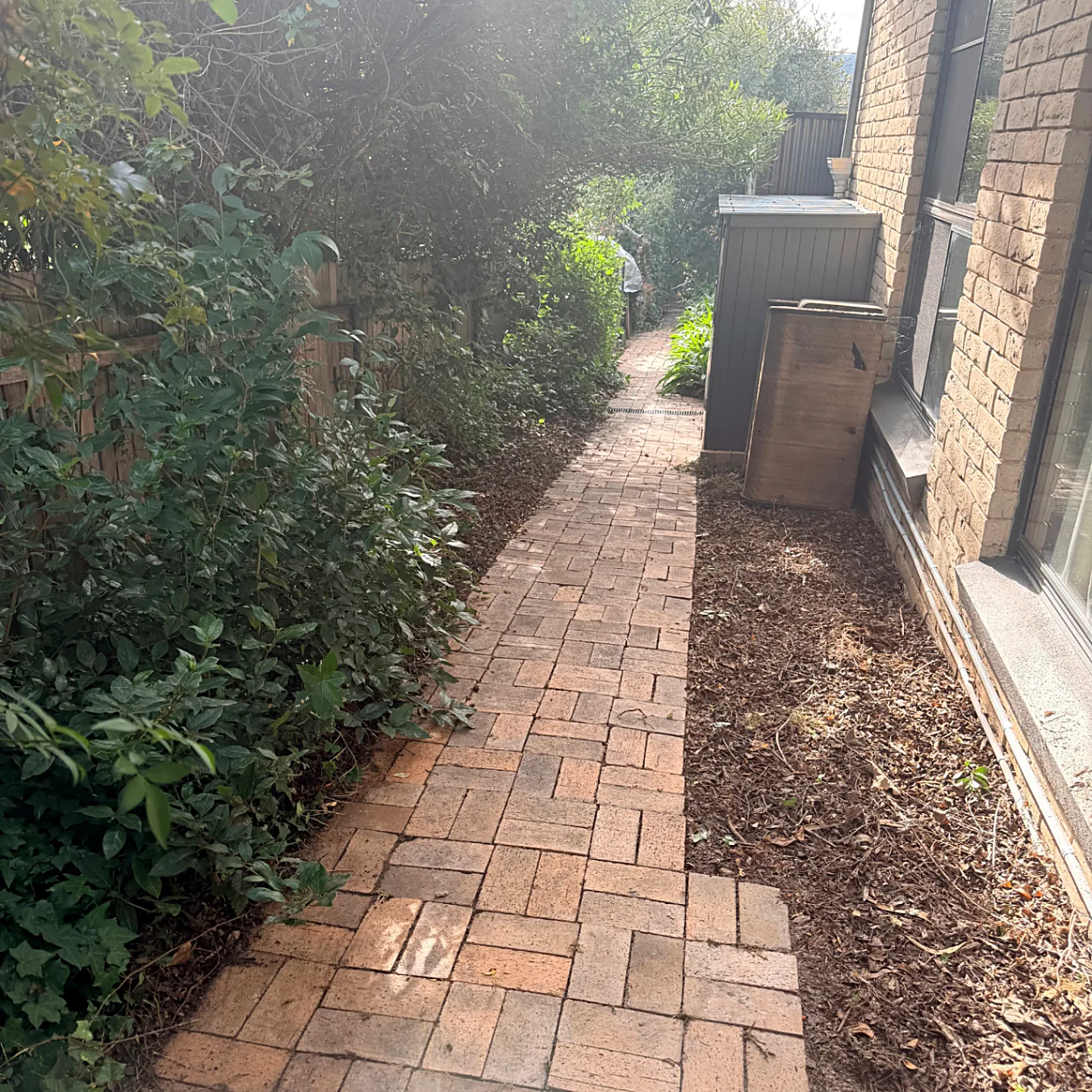 Brick paved path running alongside the house past the garden