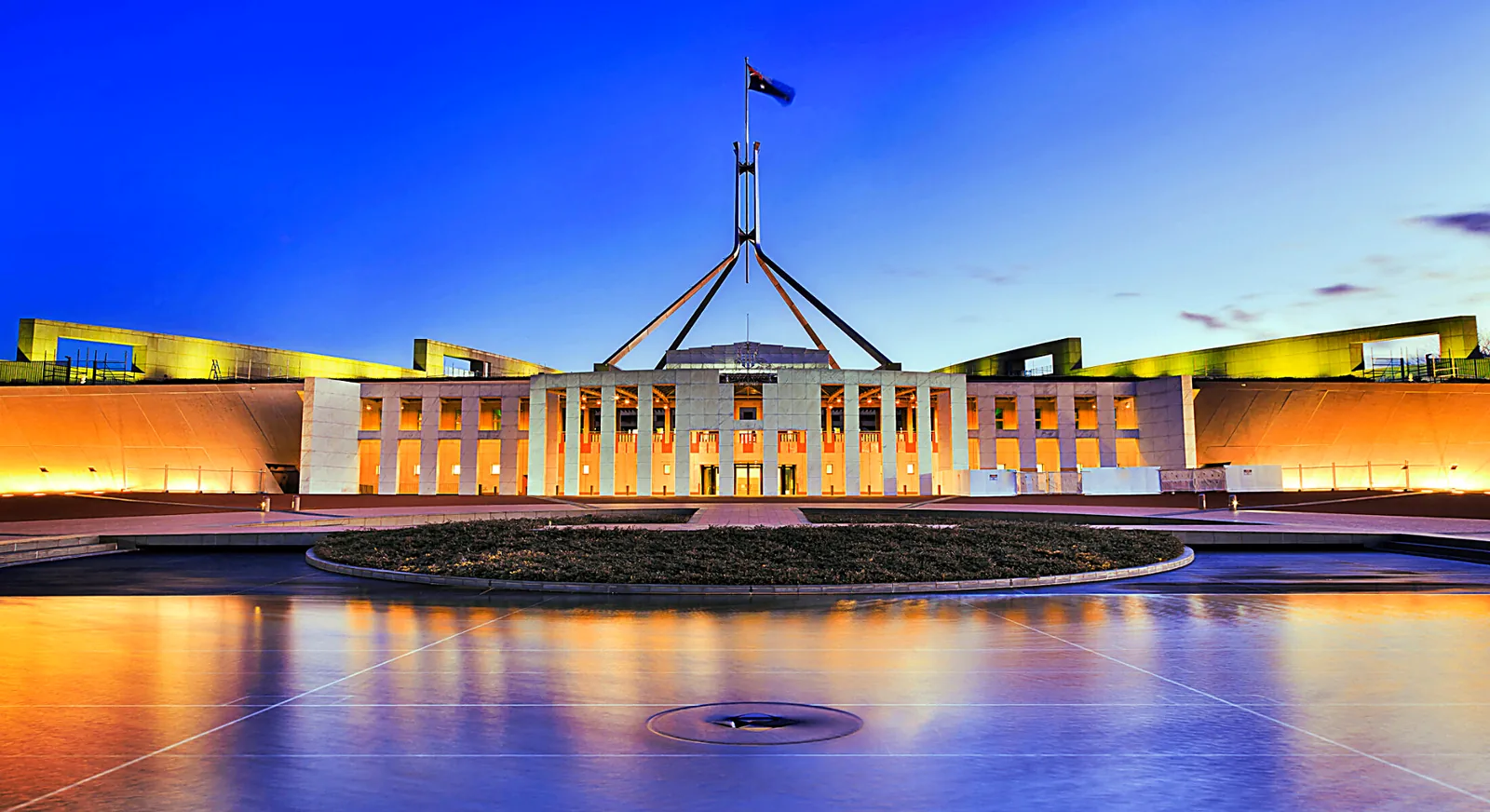 Australian Parliament House lit at dusk with the flag mast rising above the facade