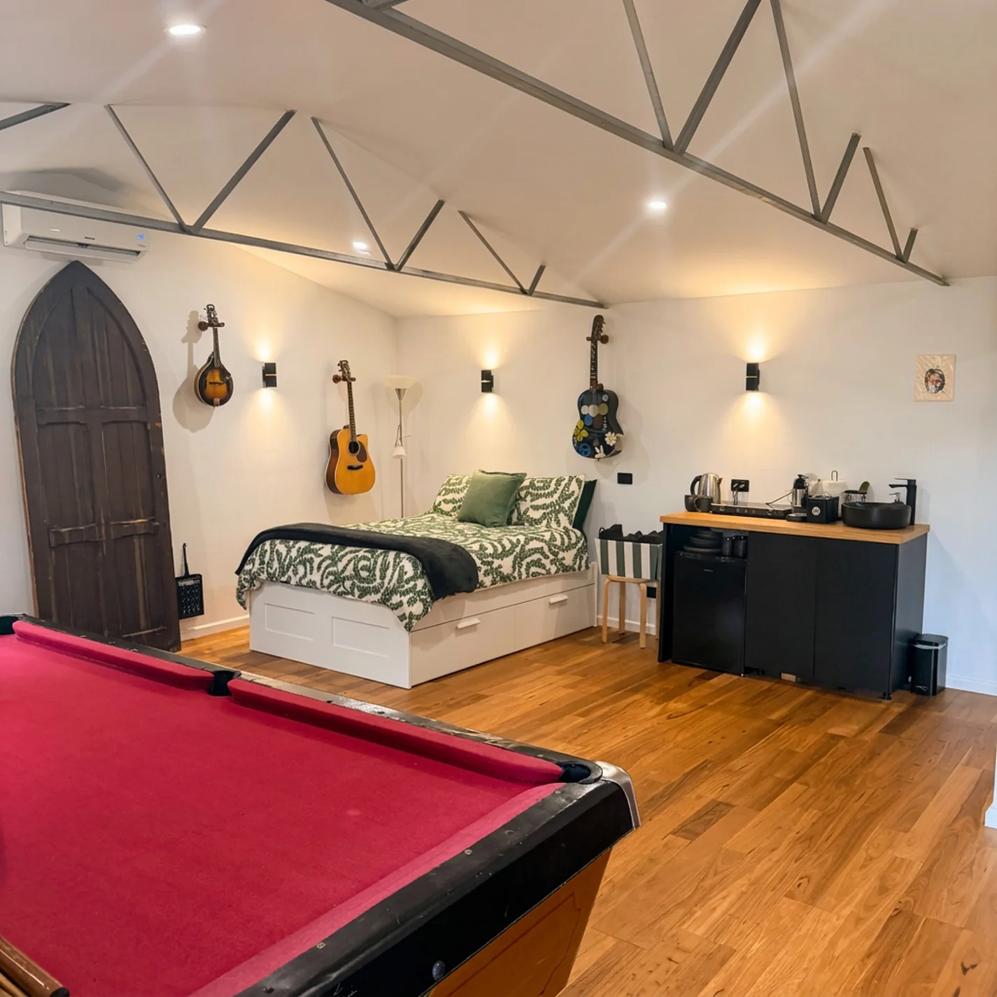 Inside Mustang Studios — queen bed, guitars on the wall, pool table and kitchenette under a vaulted ceiling